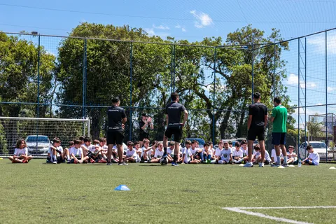 Turma sentada no gramado, com os professores em pé ao fundo, no campo do Clube URCA