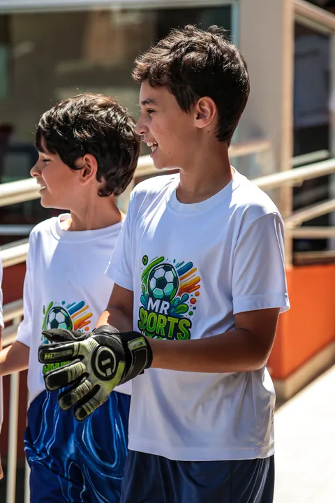 Dois meninos de camiseta branca, um deles de luvas de goleiro