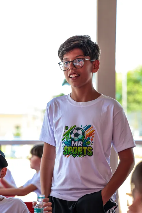 Menino de óculos e camiseta da MR Sports sorri em pé