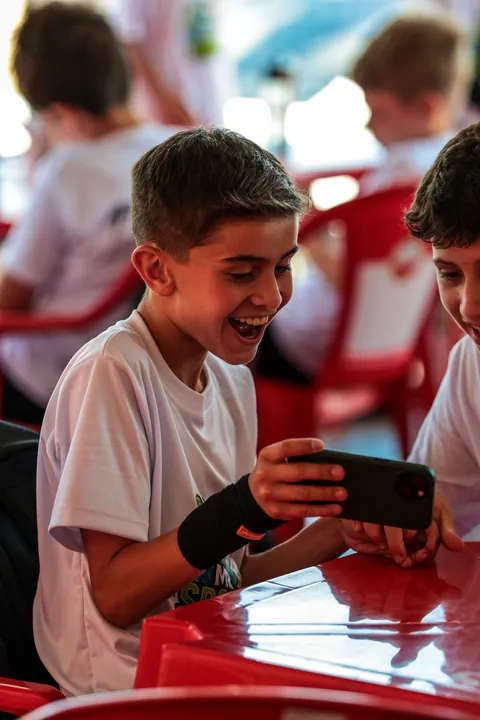 Meninos riem olhando para um celular em uma mesa vermelha