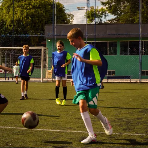 Menino corre com a bola enquanto colegas acompanham
