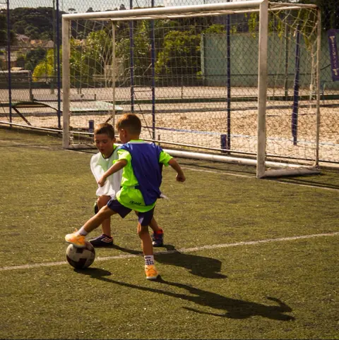 Menino conduz a bola em frente ao gol com outro jogador marcando