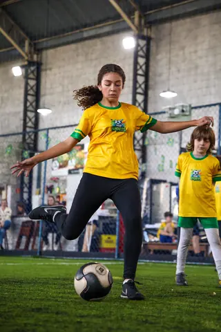 Menina de camiseta amarela prepara o chute no campo coberto