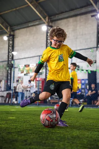 Menino de camiseta amarela da MR Sports chuta a bola no campo coberto da Arena Anita