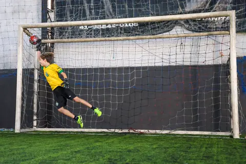 Goleiro se estica no ar para defender a bola no canto do gol