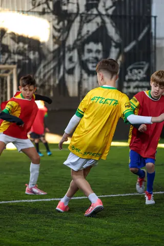 Jogo entre as turmas, com crianças de amarelo e de vermelho disputando a bola