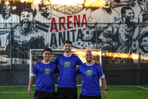 Três professores da MR Sports de camiseta azul em frente ao gol da Arena Anita
